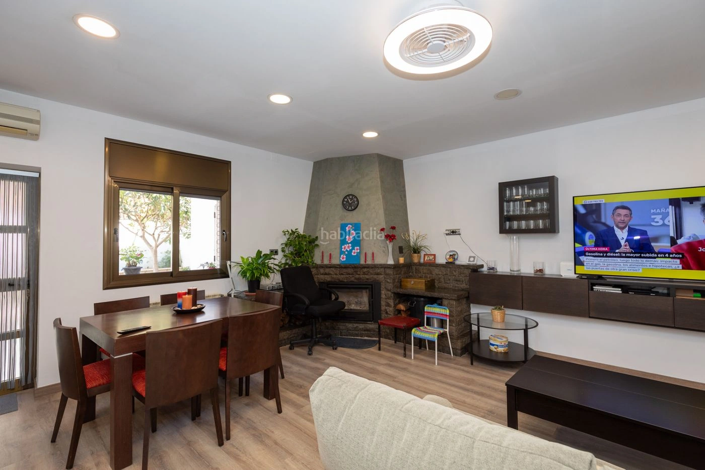 Fotografía original del salón comedor: ventana, chimenea, mesa y sofá; marca de agua conservada.